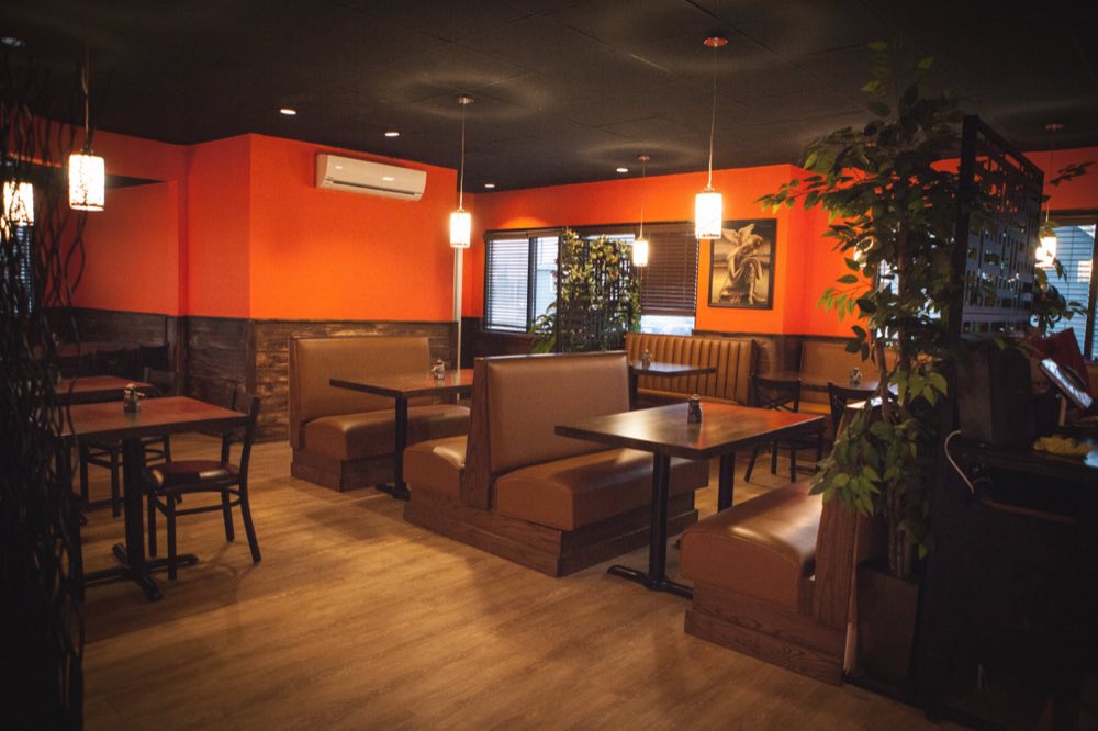 Brown leather booths and dark wood tables in the main dining room, under cylindrical pendant lamps, with orange walls above a stone wainscot.